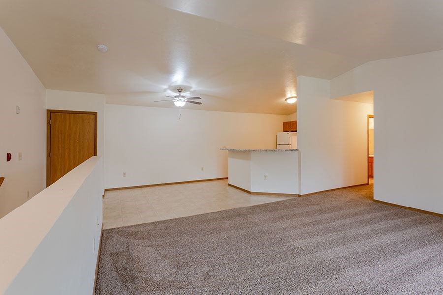 an empty living room with a kitchen and a ceiling fan