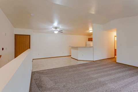 an empty living room with a kitchen and a ceiling fan
