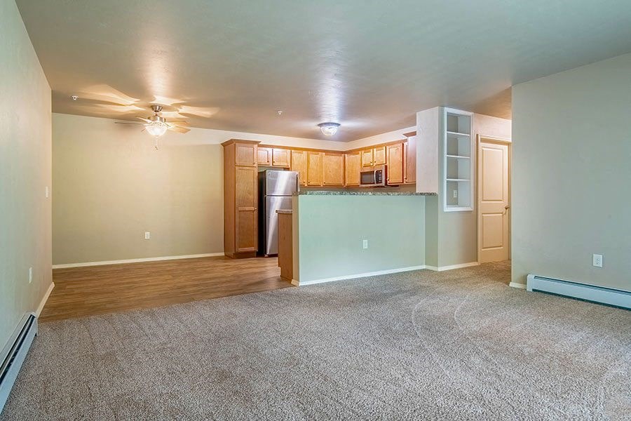 an empty living room with a kitchen and a ceiling fan