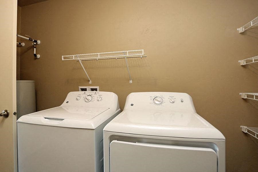two white washing machines in a bathroom with a rack on the wall