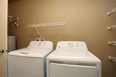 two white washing machines in a bathroom with a rack on the wall