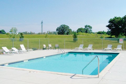 A pool surrounded by lawn chairs and trees.