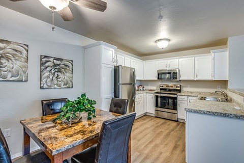 A kitchen with a table and chairs in the foreground and a refrigerator, microwave, oven, and stove in the background.
