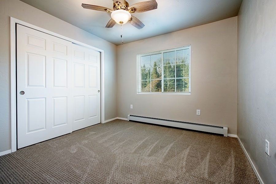 A room with a carpeted floor, a ceiling fan, and a window with blinds.