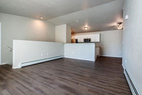 A spacious room with wooden flooring and a kitchen area in the background.