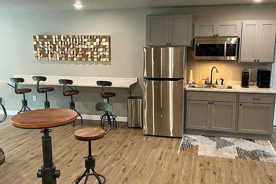 A kitchen with a refrigerator, bar stools, and a wooden table.