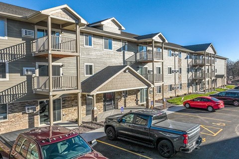 A red pickup truck is parked in a parking lot in front of a building with a balcony.