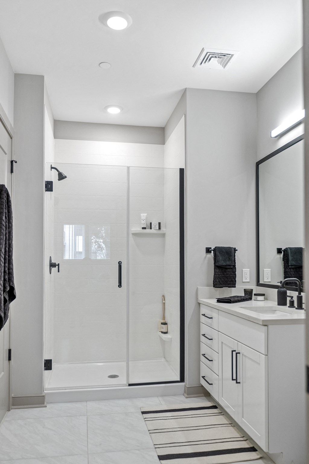 a bathroom with a glass shower stall and white cabinetry at The Harrison, Newtown Square, 19073