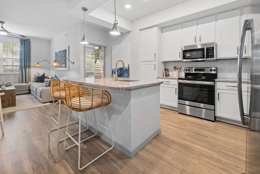 an open kitchen and living room with an island and chairs at Inspira, Naples, FL