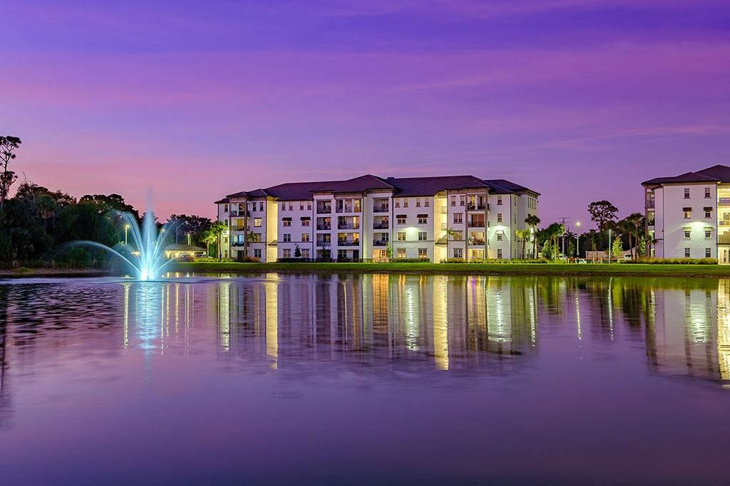 a fountain in a lake with an apartment building at dusk at Inspira, Naples, FL, 34113