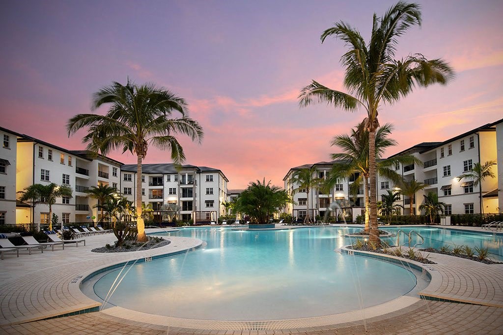 a large swimming pool with palm trees at sunset at Inspira, Naples, FL