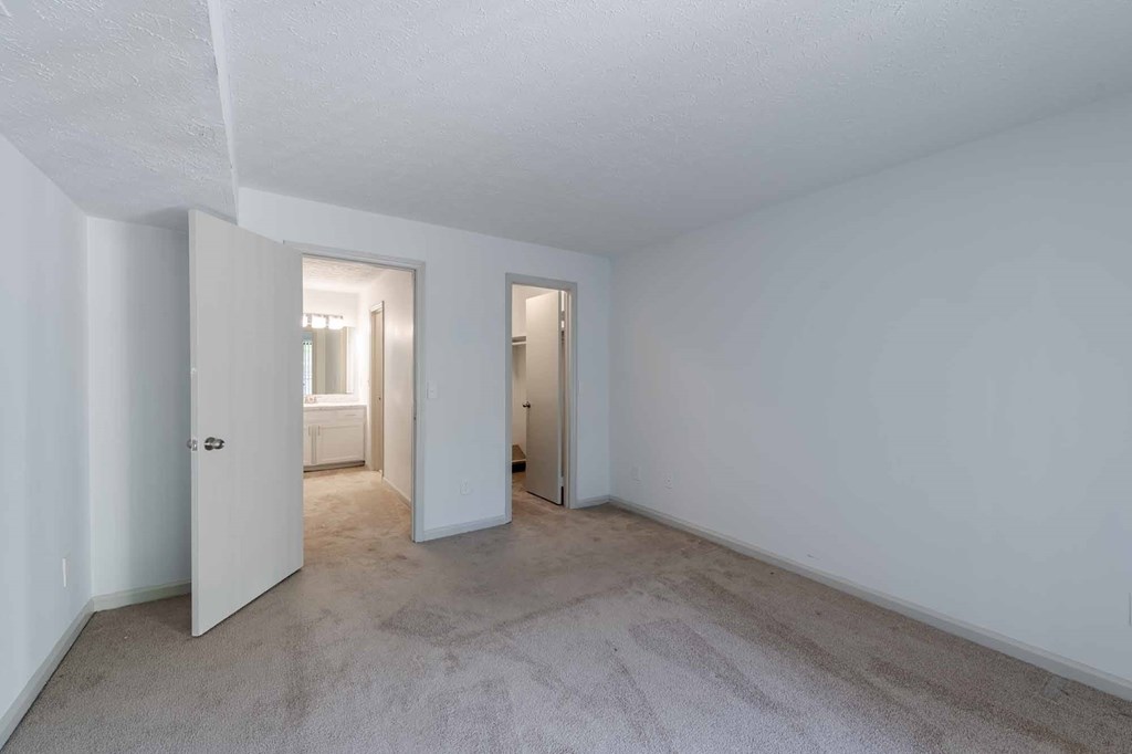 A room with white walls and carpeted floor with a doorway leading to another room.