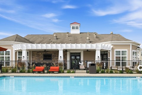 A pool in front of a clubhouse with a white fence.