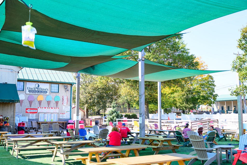 A group of people are sitting under a green canopy at an outdoor picnic area at Madison Prickett Preserve, Yardley, PA