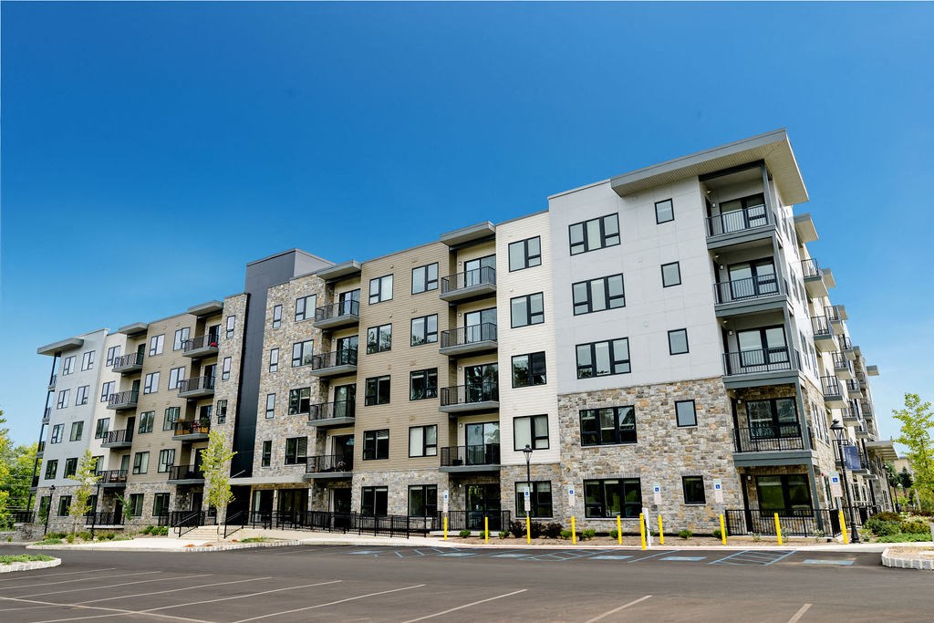 an apartment building on a street corner with a blue sky at The Harrison, Newtown Square, PA, 19073