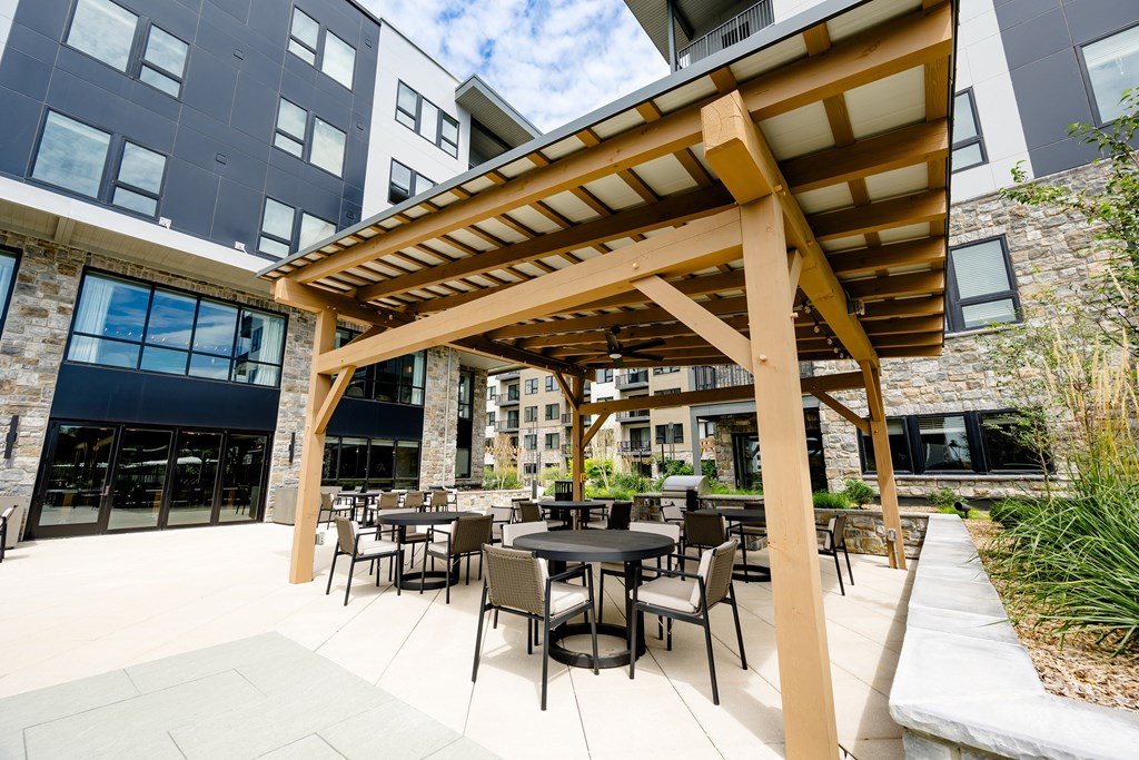 an outdoor patio with a pergola and tables and chairs at The Harrison, Newtown Square, PA, 19073