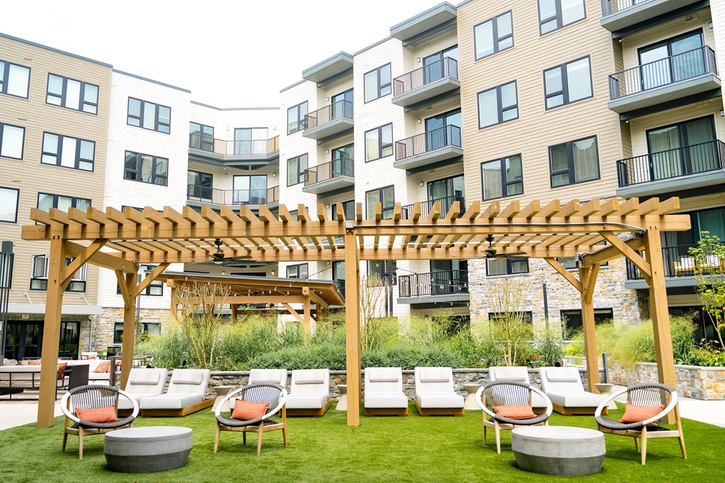 an outdoor lounge area with lounge chairs and a pergola in front of an apartment building at The Harrison, Newtown Square, 19073