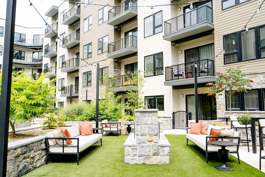 an outdoor lounge area with couches and a fire pit in front of an apartment building at The Harrison, Newtown Square, PA