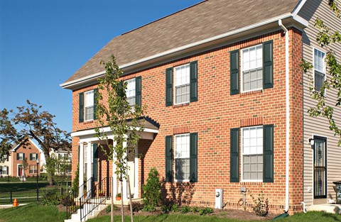 a brick house with green shutters and a tree in the yard