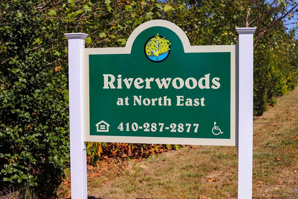 a sign for riverwoods at north east with trees in the background