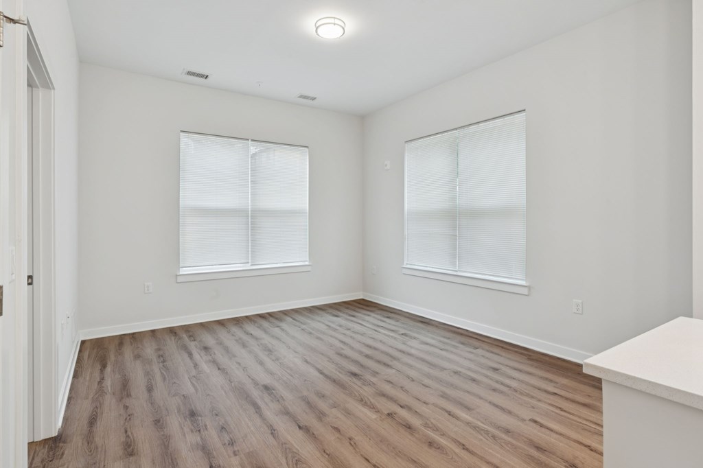 A room with wooden flooring and two windows.