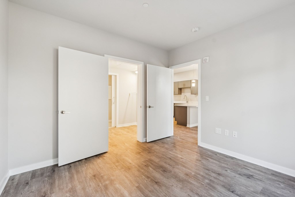 A room with white walls and wooden flooring with two open doors.