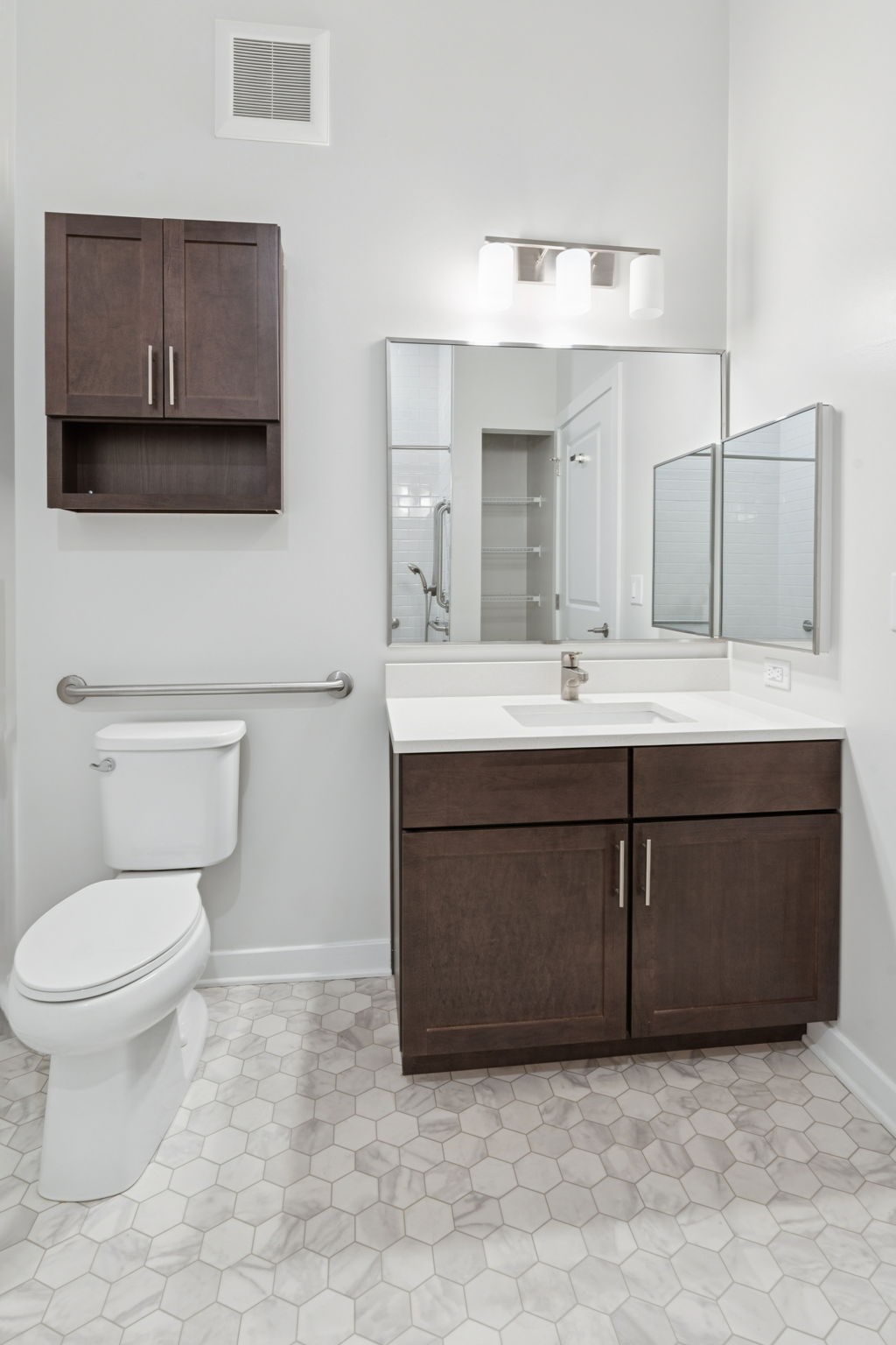 A white toilet sits in a bathroom with a white sink and brown cabinets.