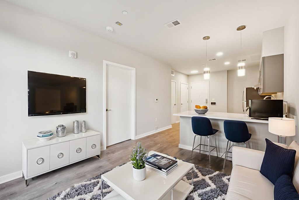 A living room with a white couch, a white coffee table, and a white cabinet with a flat screen TV mounted on the wall.