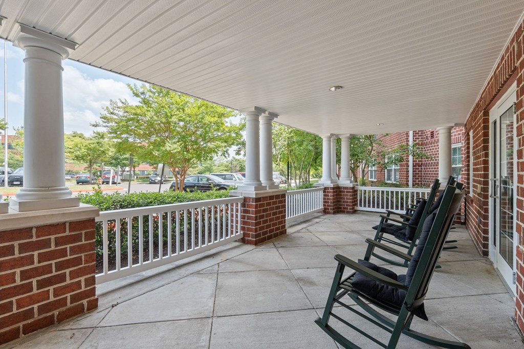 a front porch with rocking chairs and a brick building in the background