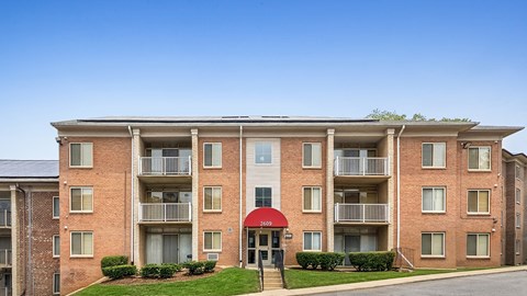 A red brick apartment building with a red awning and a green lawn in front.