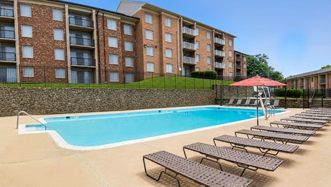 A swimming pool with sun loungers and a red umbrella in front of a brick building.