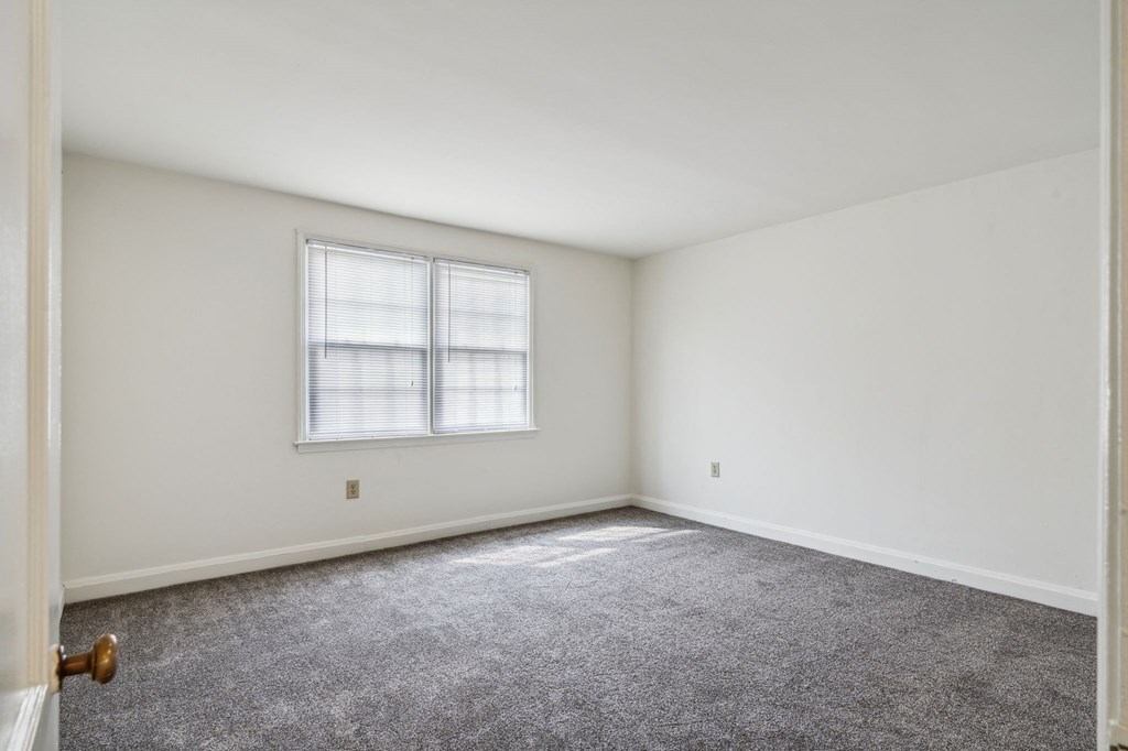 a bedroom with white walls and carpet and a window