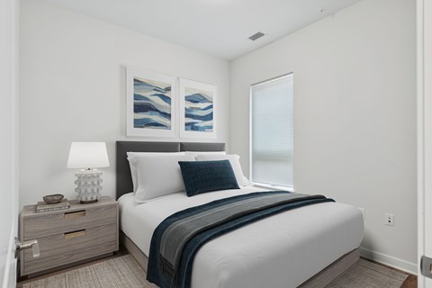 A bedroom with a bed, nightstand, and artwork on the wall.