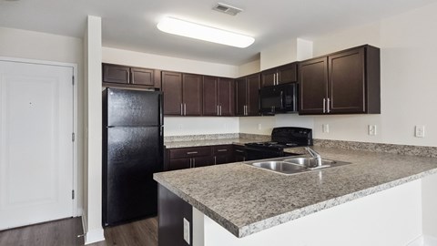 A kitchen with a black refrigerator and brown cabinets.