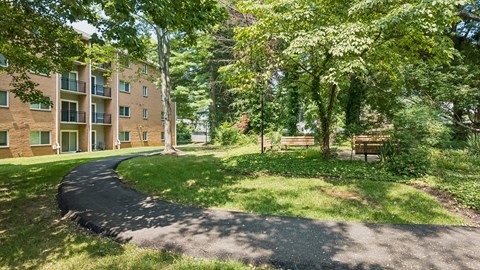 A paved walkway leads through a grassy area to a building with balconies.