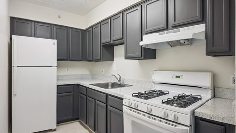 A white refrigerator sits in a kitchen with dark grey cabinets.