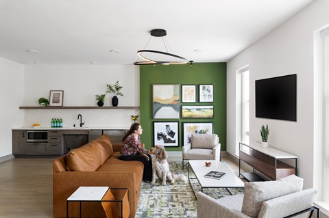 A woman is sitting on a couch with a dog in a living room.