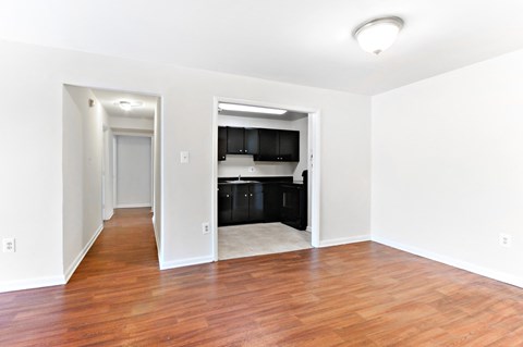 an empty living room with a hard wood floor and a kitchen
