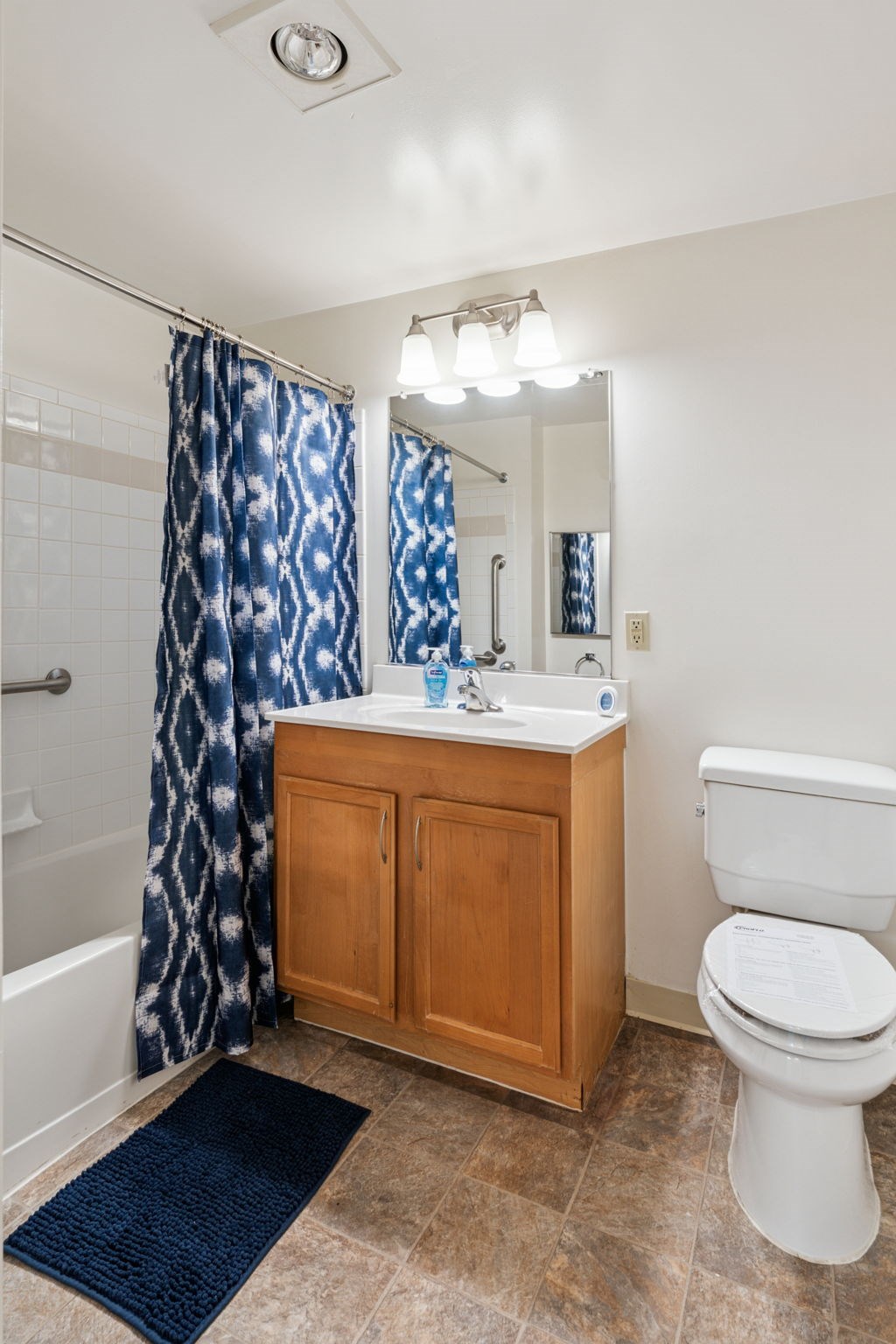 A bathroom with a white toilet, a sink with a wooden cabinet, and a blue shower curtain.