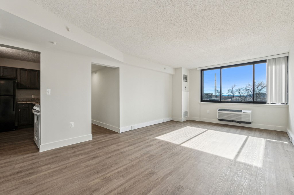 A spacious living room with a large window and a wooden floor.