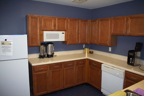 Spacious community kitchen fully equipped with a white refrigerator, dishwasher, microwave, and small appliances.