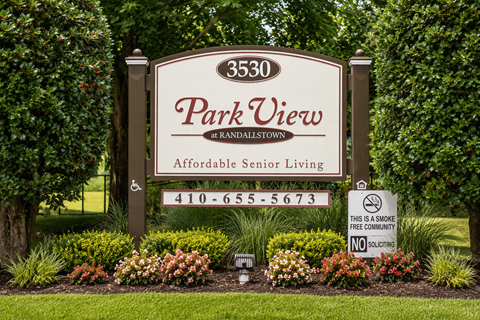 A sign for Park View at Randalstown, an affordable senior living community, is displayed in front of a green hedge.