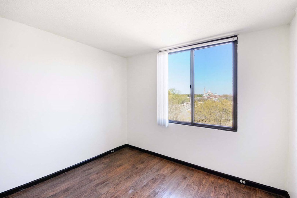 spacious bedroom with a large window and hardwood floors