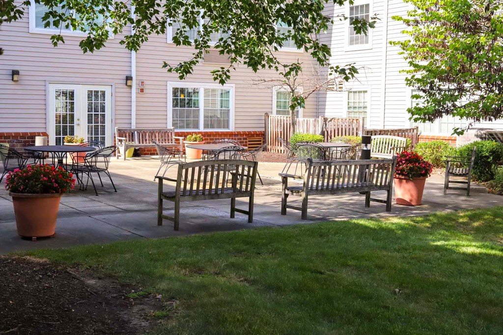 A patio with chairs and tables is surrounded by a green lawn.