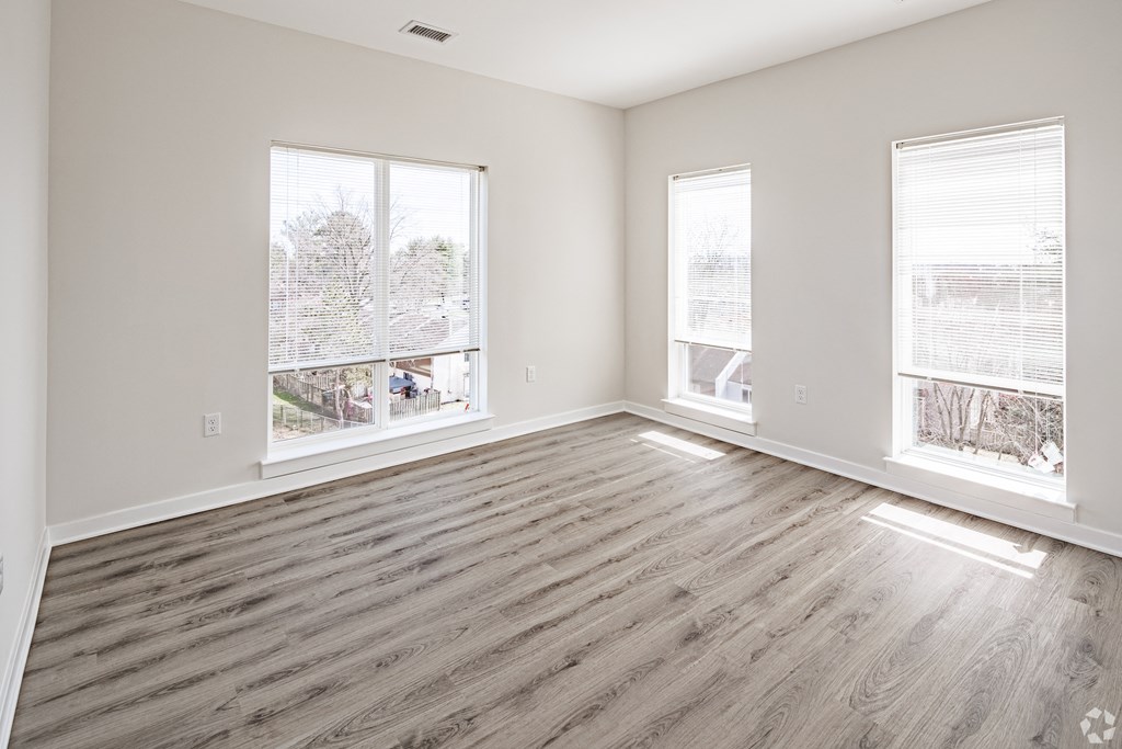 an empty living room with wood floors and three windows