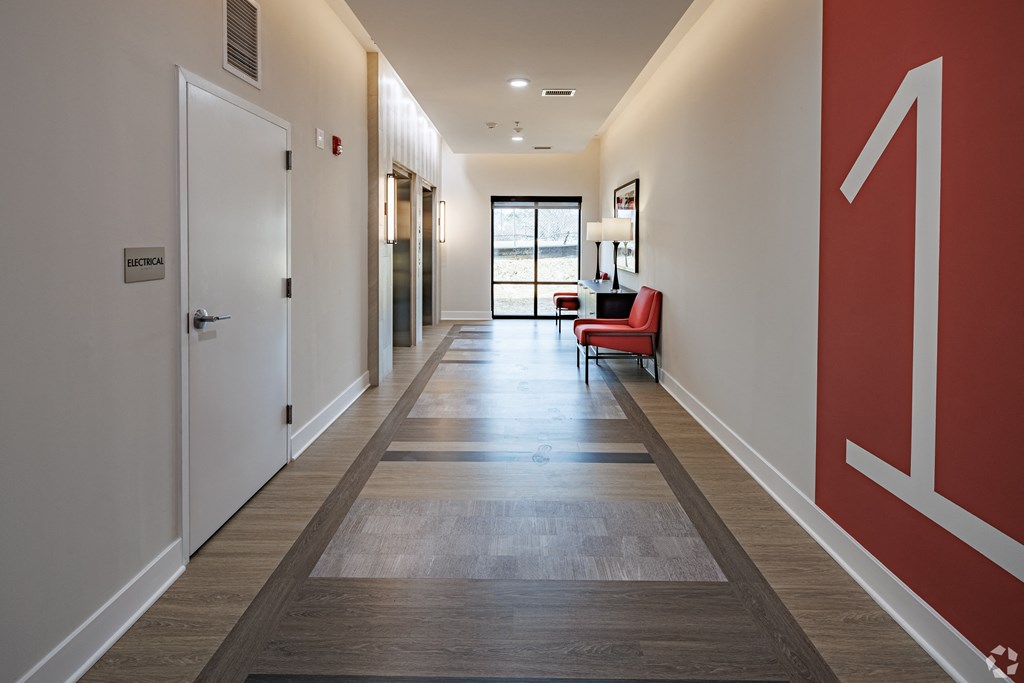 a long hallway with red and white walls and wood flooring and a red chair
