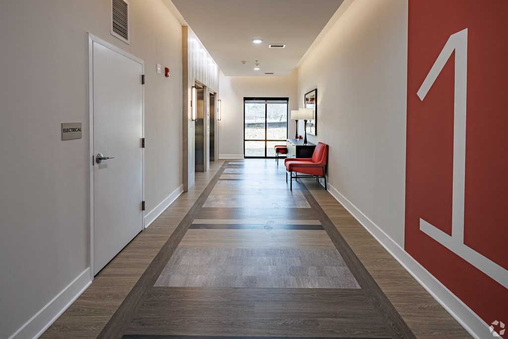 a long hallway with red and white walls and wood flooring and a red chair