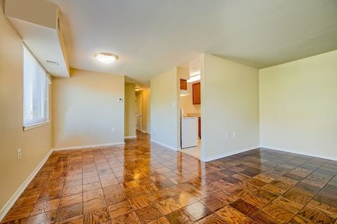 an empty living room with wood flooring and a kitchen