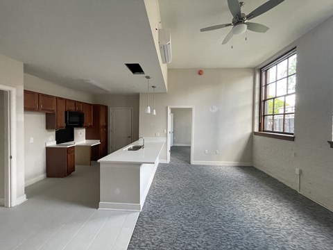an empty living room with a kitchen and a ceiling fan