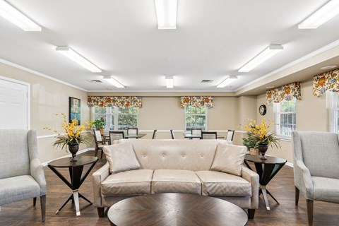 A living room with a beige sofa, two chairs, and two tables with vases of flowers.